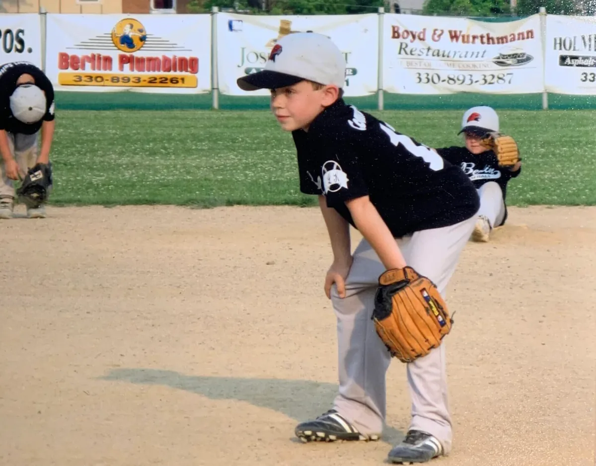 A young Logan Miller focused on the next play, wearing his baseball uniform and holding his glove